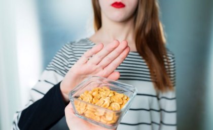 A bowl of peanuts is offered to a young woman who holds up her hand to say no. 